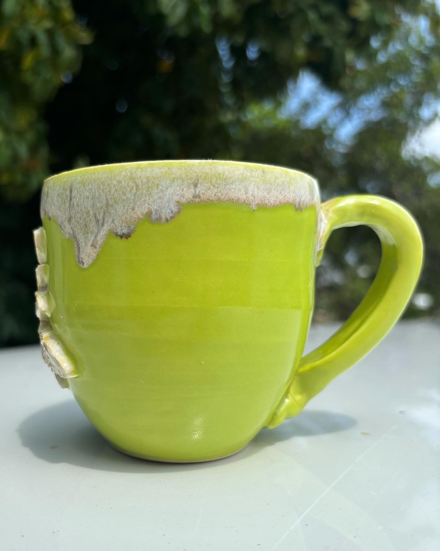 Photo of a bright green ceramic mug with a warm, creamy glaze with brown flecks dripping from the rim.