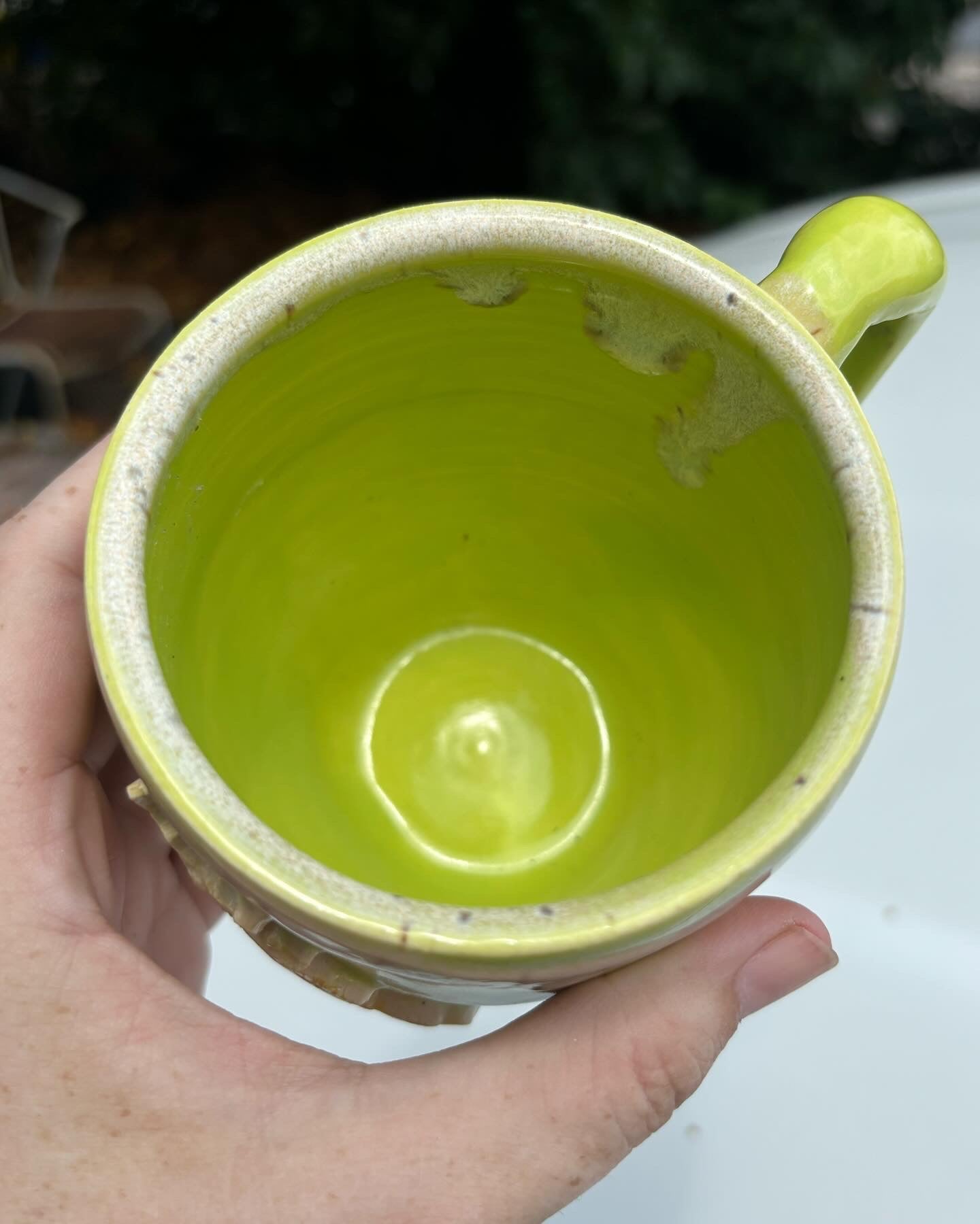 Photo of the top view of a mug with bright green glaze and a rim of warm cream glaze with dark flecks.