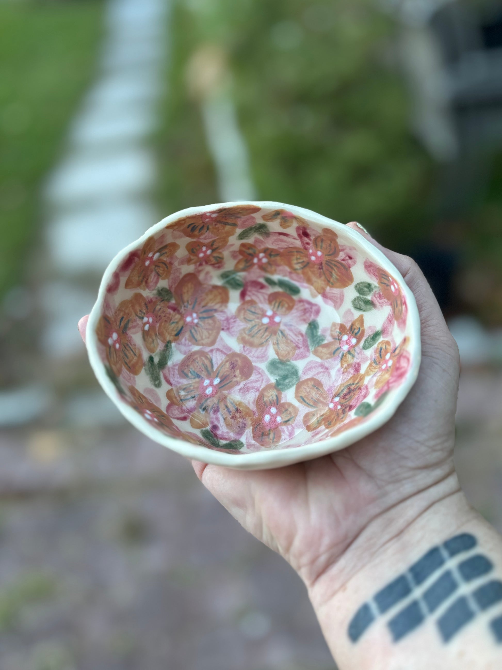 Photo of the artist holding a small round ceramic dish painted with red and orange blossoms.