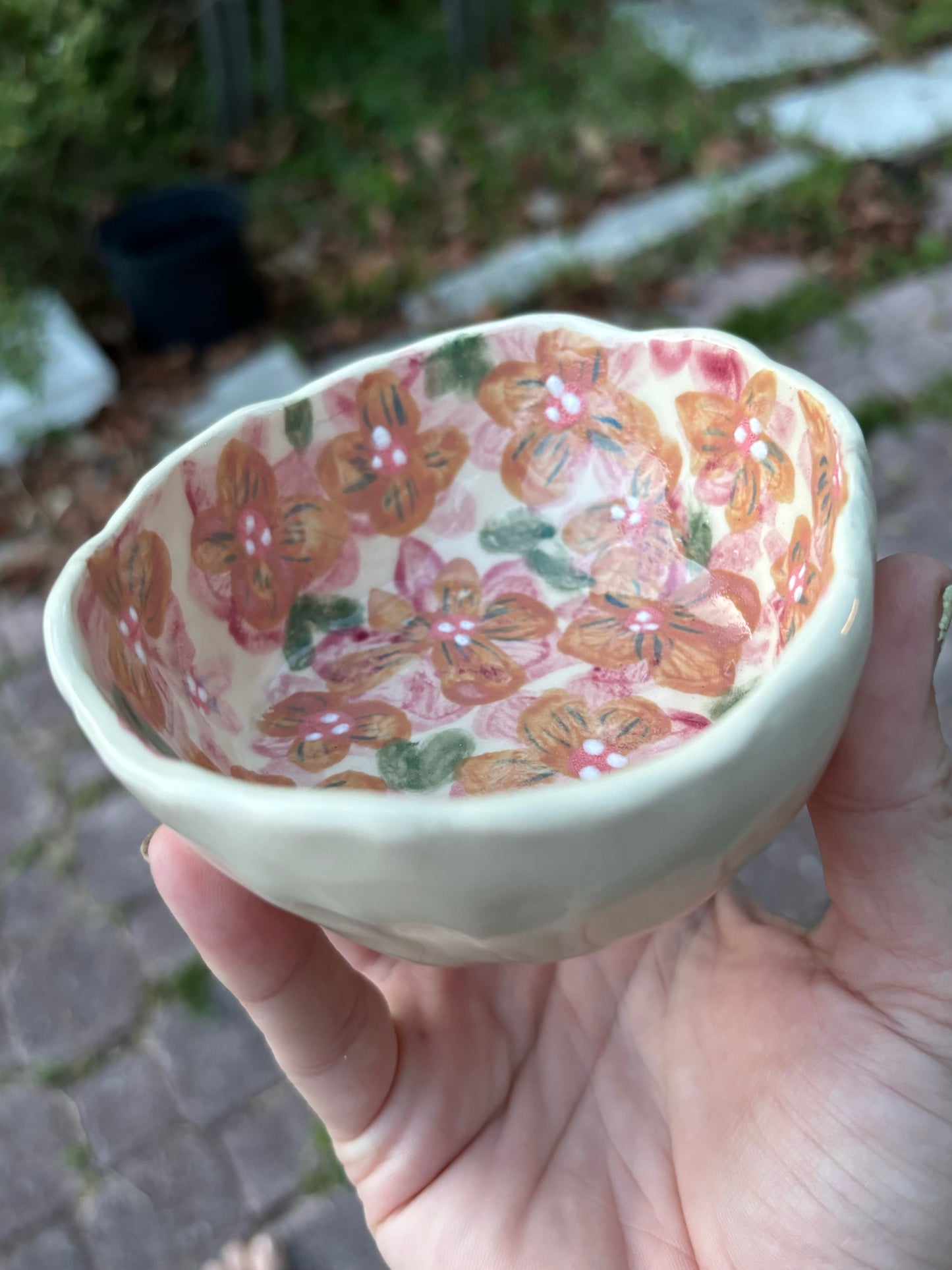 Photo of the artist holding a small round ceramic dish painted with red and orange blossoms.