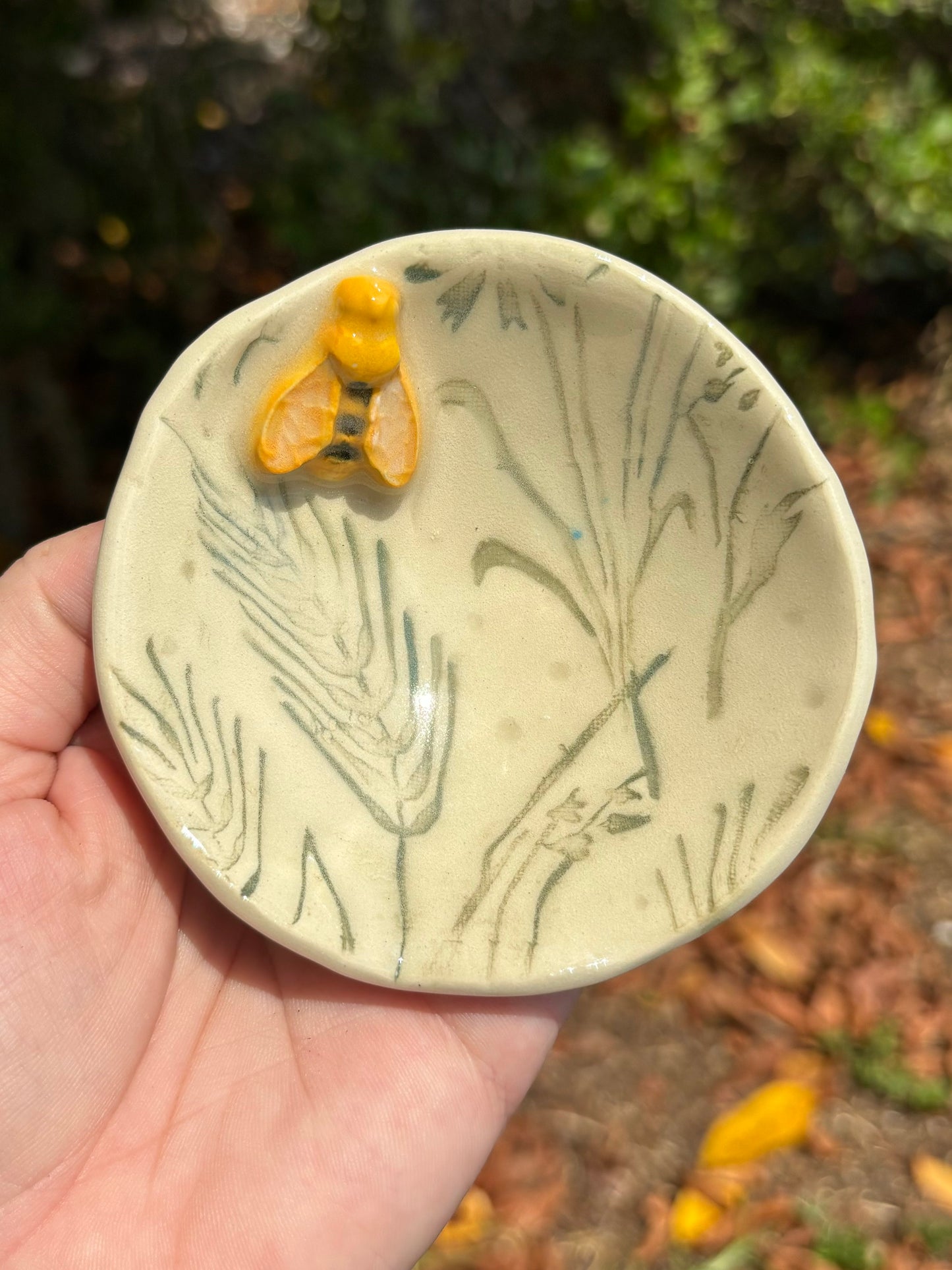 Photo of a small bee themed dish with a sculptural yellow and black bee set on a dish with inlaid green grasses.