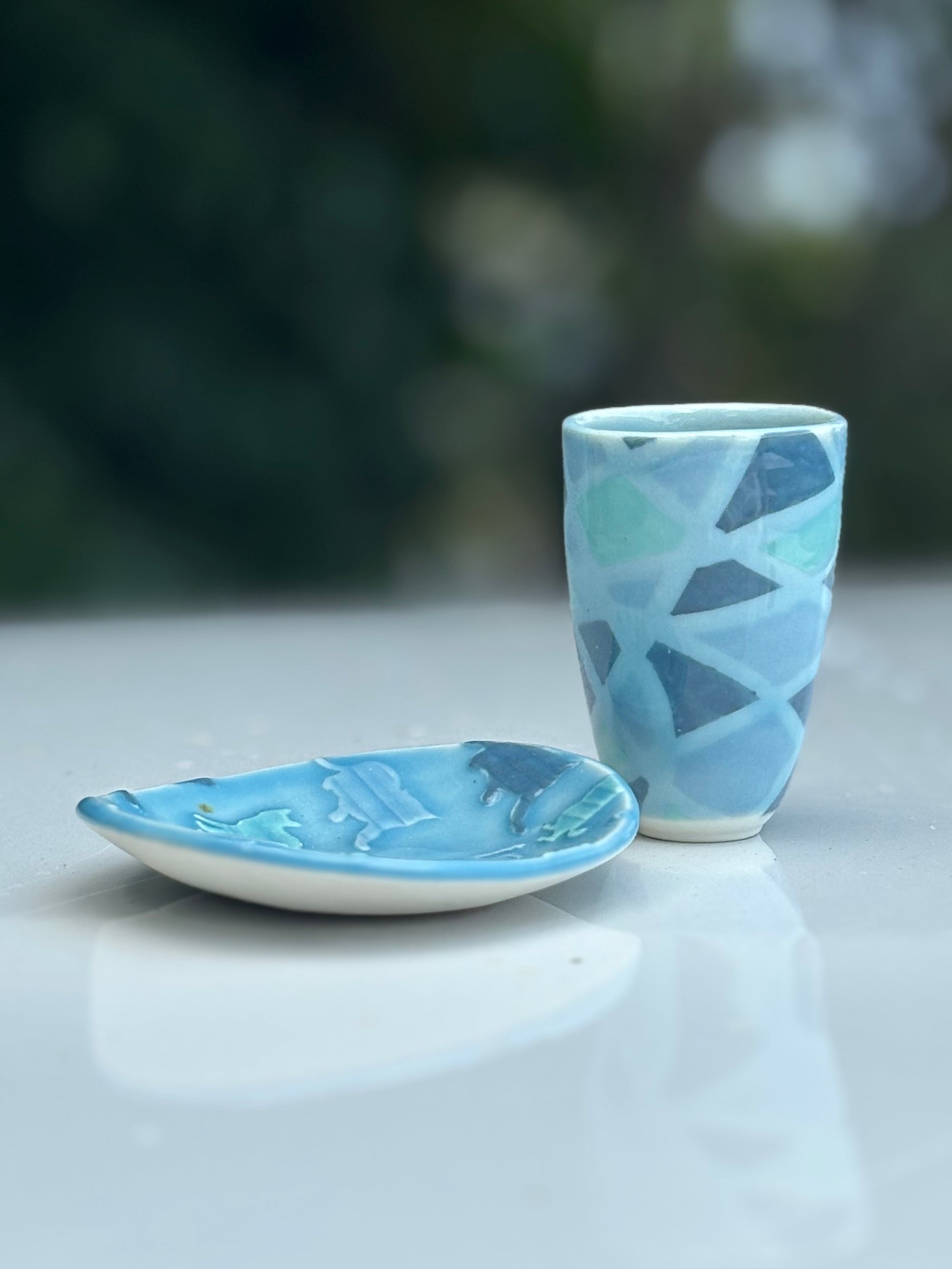 Photo of a small dish and matching cup in shades of blue.  The dish has textured cats pressed into the clay, and the cup has stripes and lines that look like a wrapped up ball of yarn.