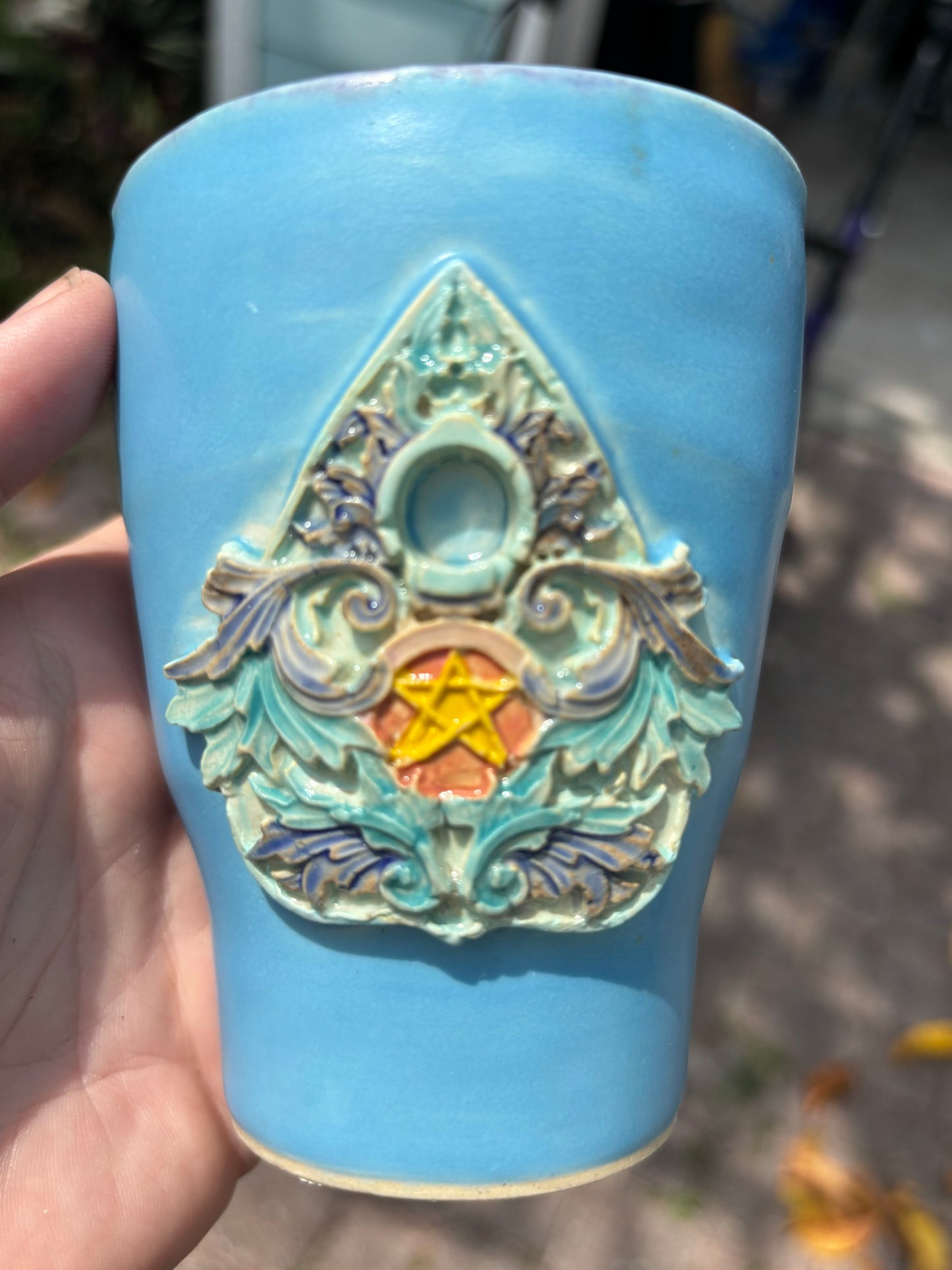 Photo of a blue mug with a ceramic ornate planchette painted in bright jewel tones.