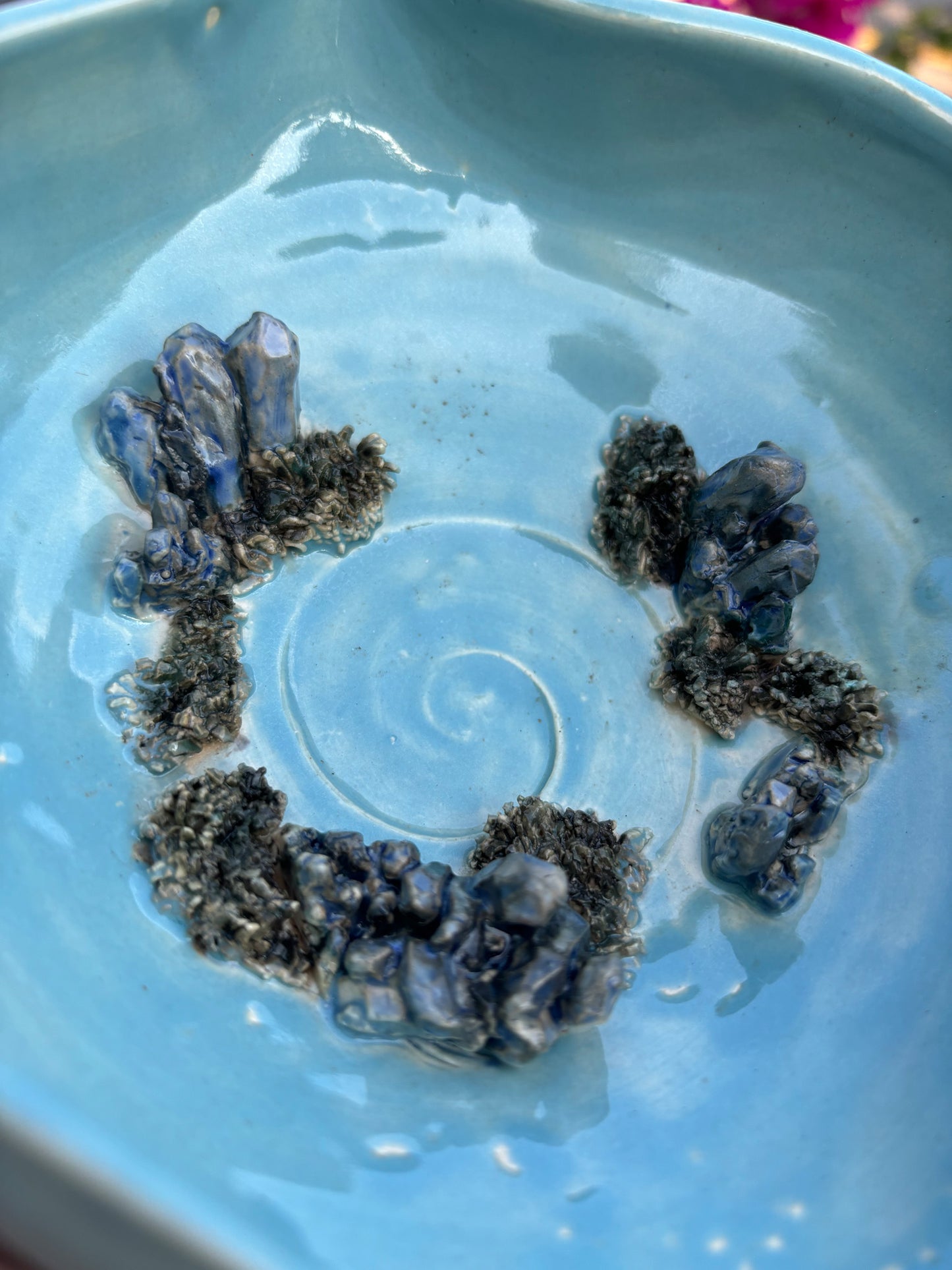 Close up photo of the bottom of a blue green bowl showing the details of ceramic crystals and moss.