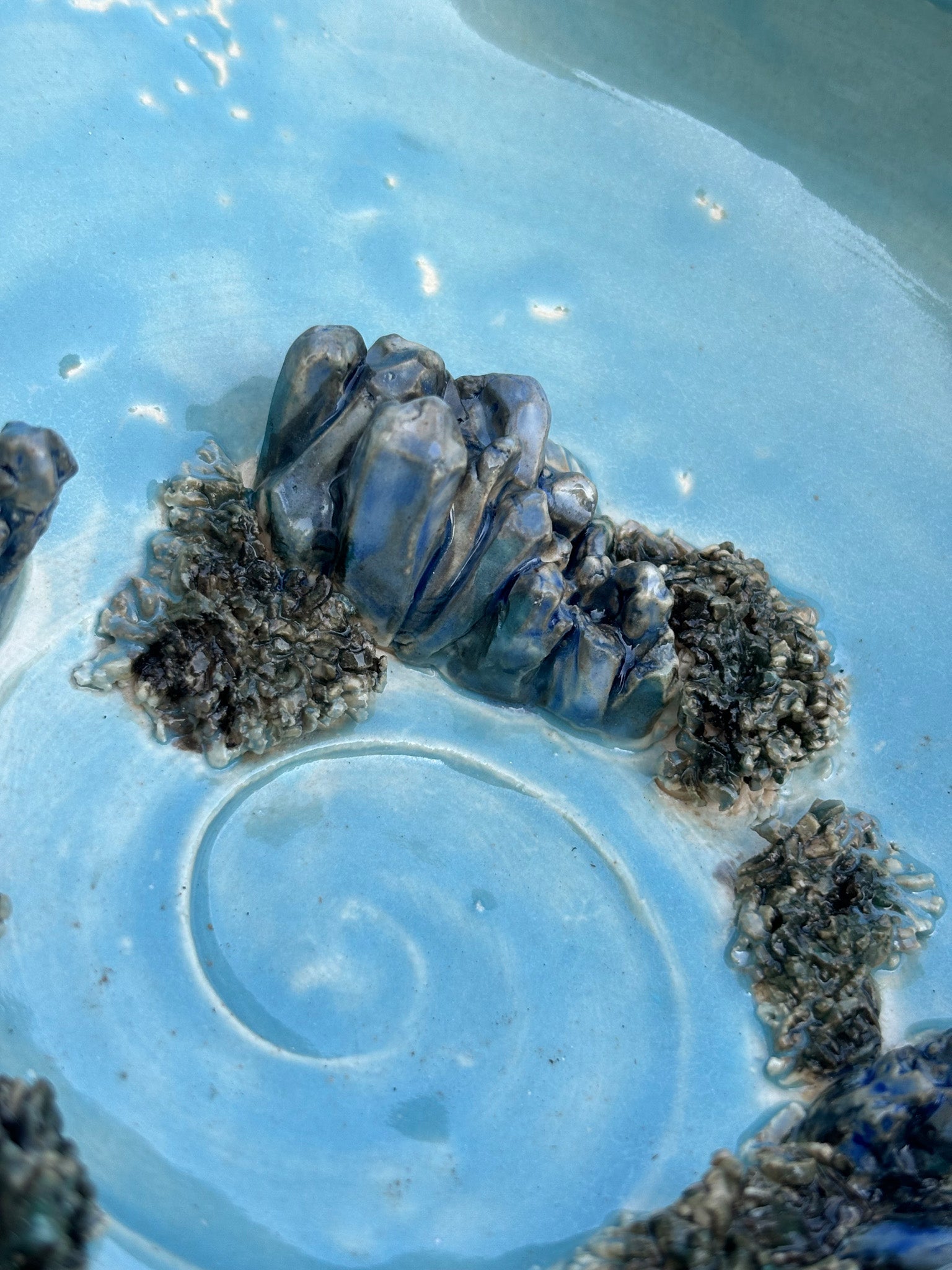 Close up detail of sculpted clay crystals and moss inside of a blue green pottery bowl with a sacred spiral in the center.