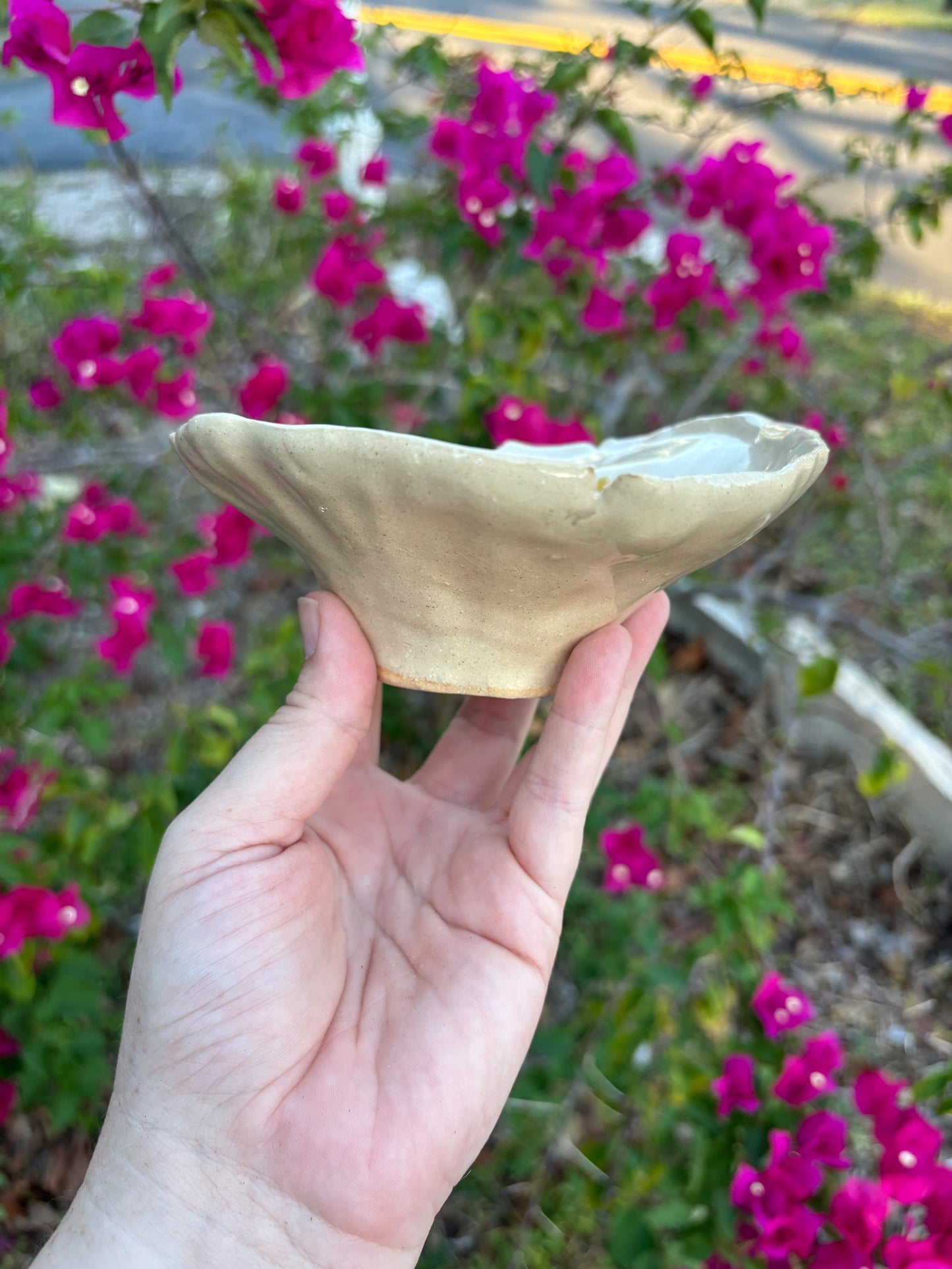 Side view of a white sculptural bowl against a background of bushes with pink flowers.