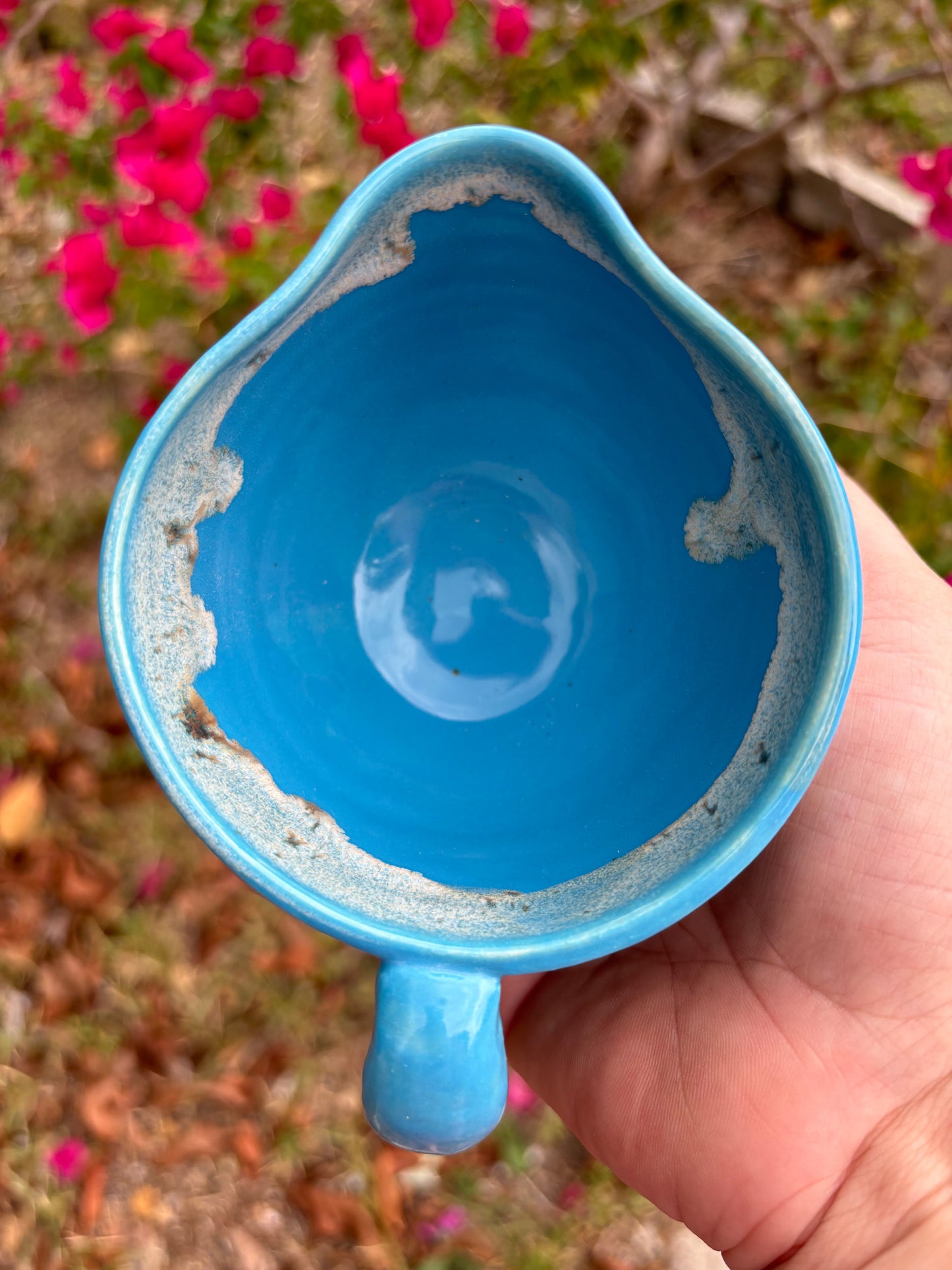 Top view of a bright blue ceramic creamer with a toasty warm marshmallow glaze around the rim.