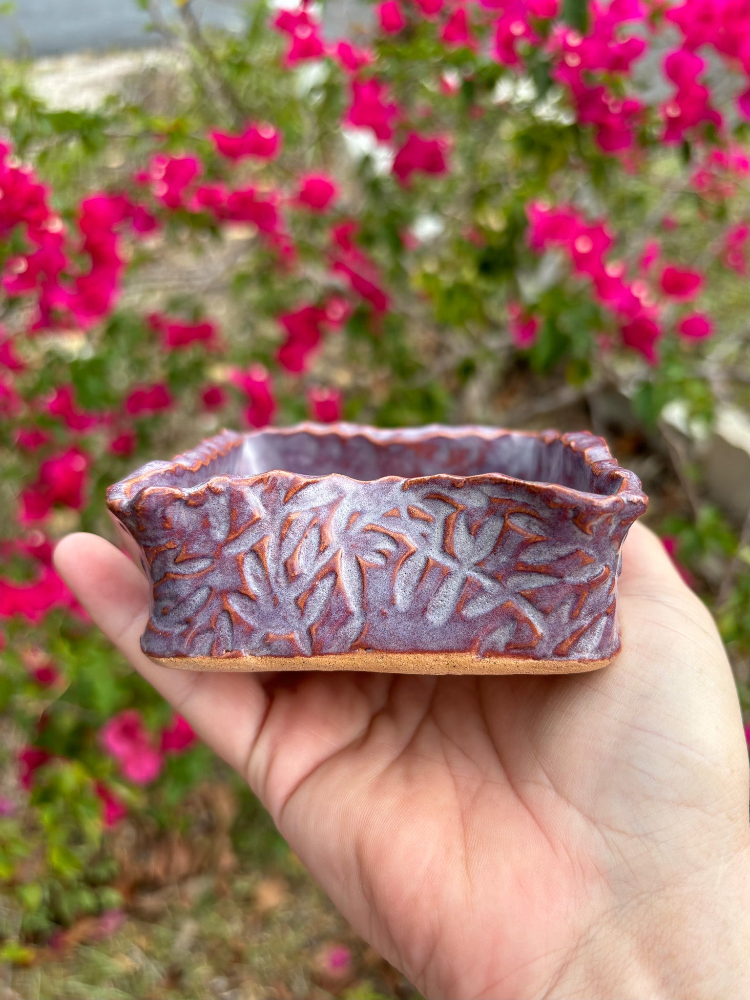 Side view of a purple ceramic box with leafy vines imprinted into the clay.