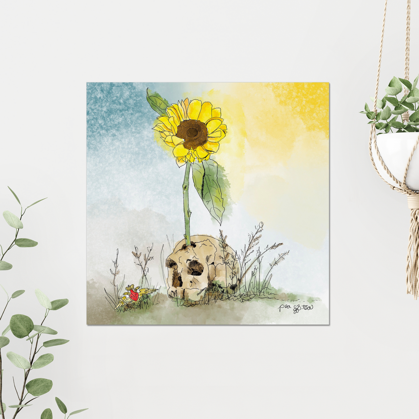 Photo of an art print featuring a sunflower growing up out of a human skull in the weeds, hanging on a white wall and  framed by green plants.